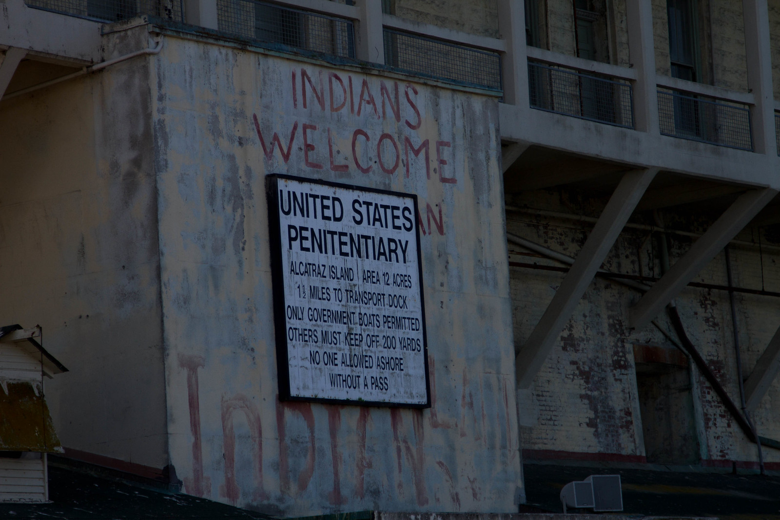 Weathered Alcatraz building with "Indians Welcome" painted above a "United States Penitentiary" sign.