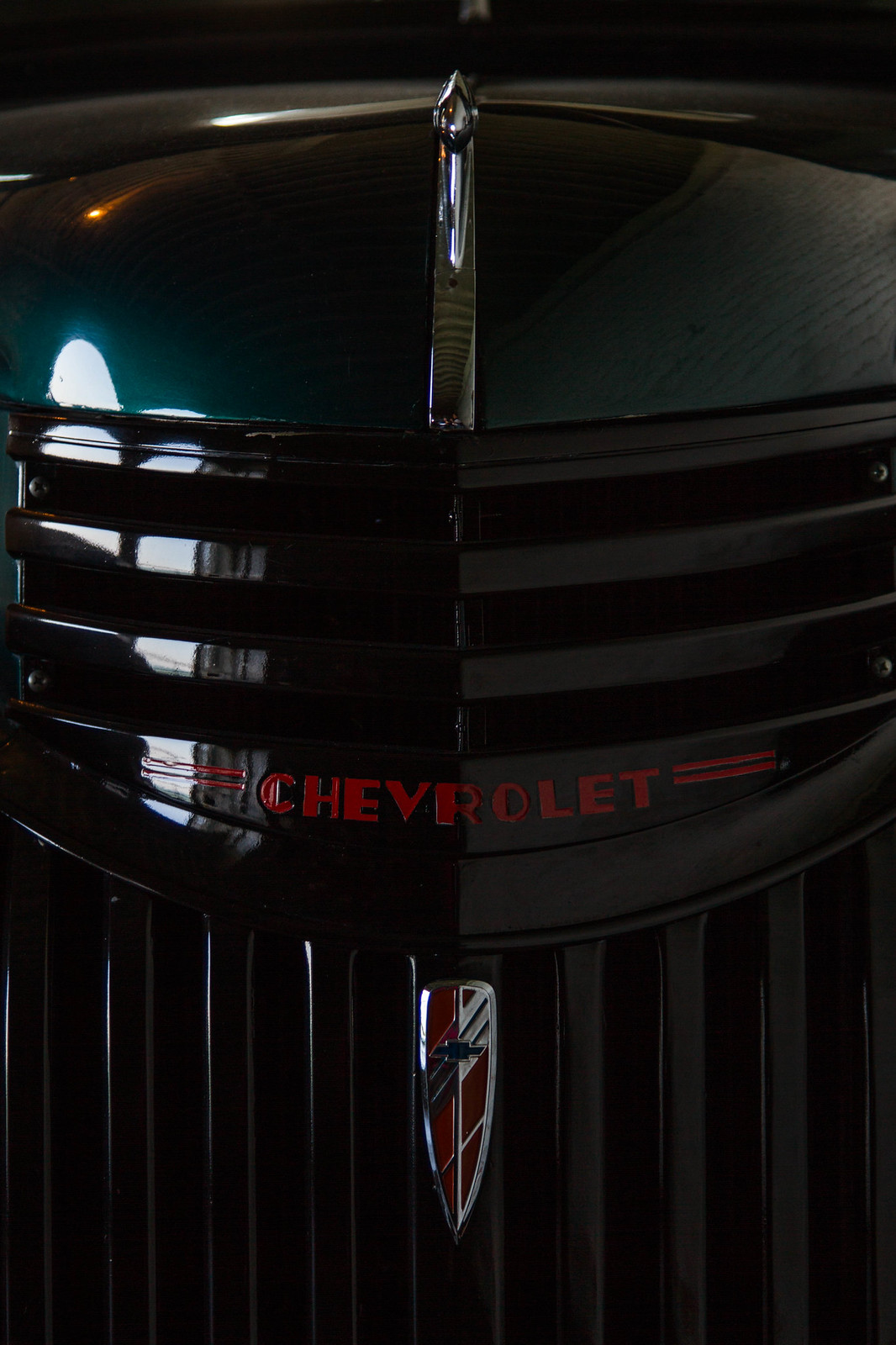 Close-up of a vintage dark green Chevrolet truck's chrome grille and red "CHEVROLET" badge.