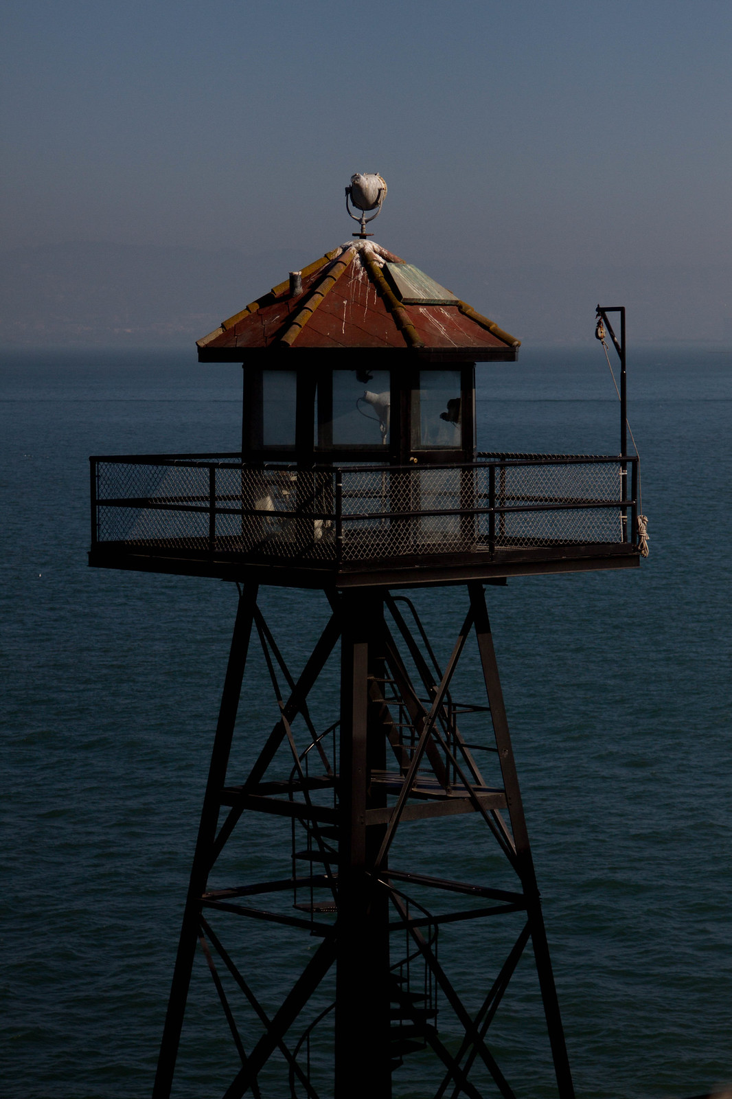 A weathered guard tower with a searchlight and red-tiled roof stands against the bay at Alcatraz.