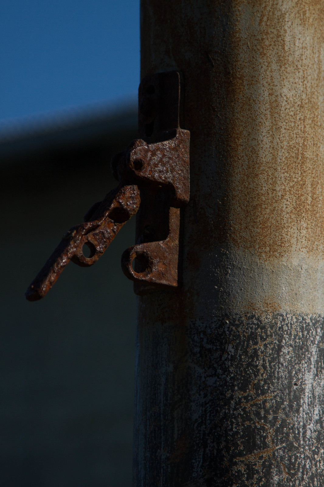 Rusted metal latch and clasp on a weathered steel pole, sea and blue sky behind.