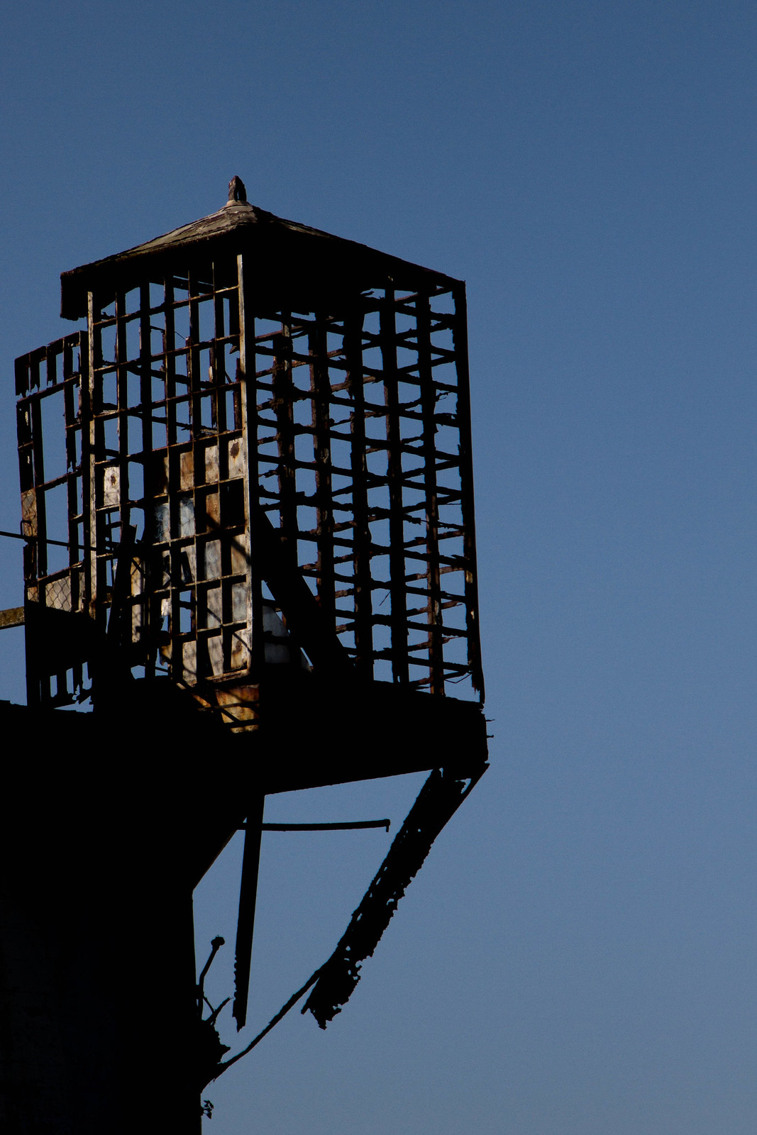 A rusted, cage-like guard tower silhouetted against a clear blue sky at Alcatraz.
