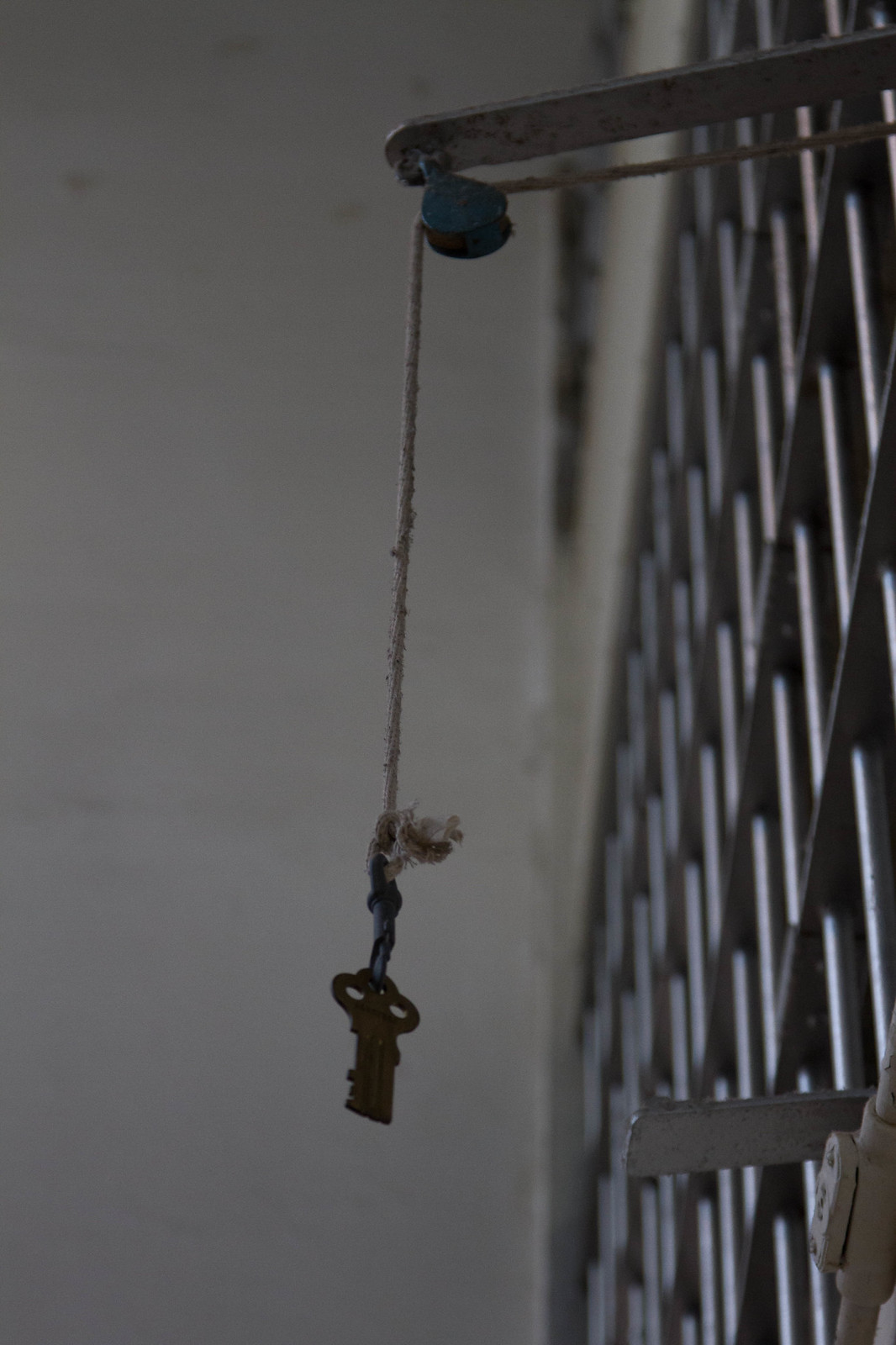 An old brass key hanging on a rope-and-pulley over a white cell block railing at Alcatraz.