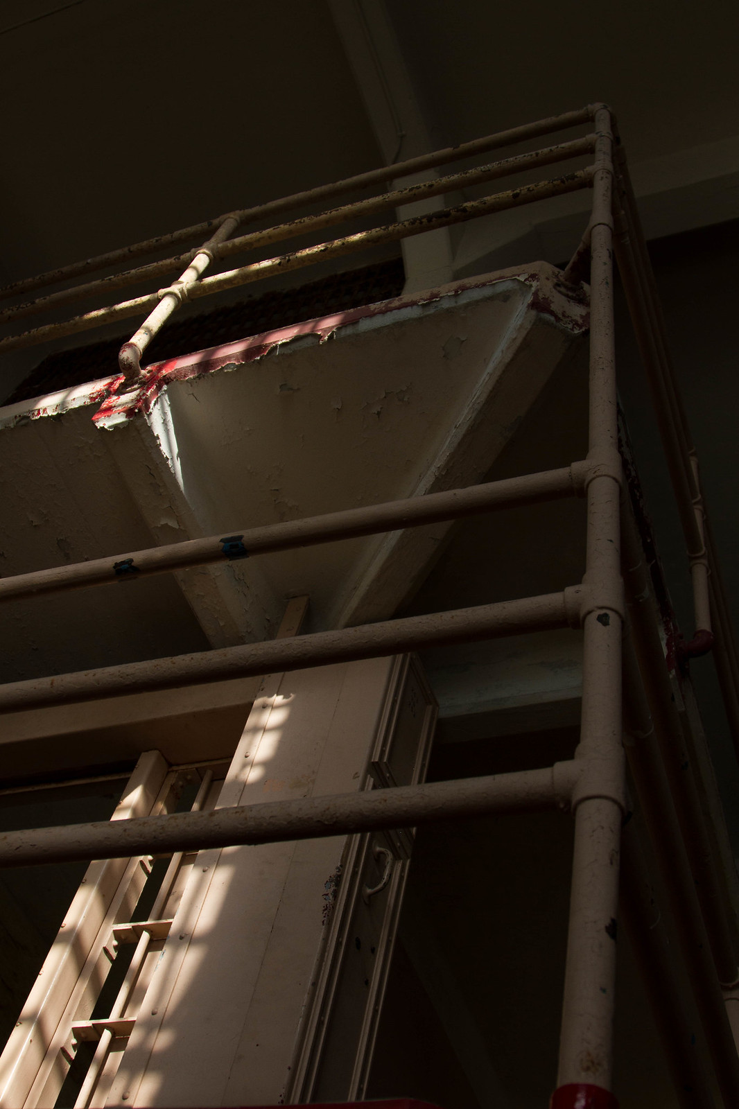 Sunlight falls across weathered metal railings and peeling paint on a multi-tiered Alcatraz cell block.