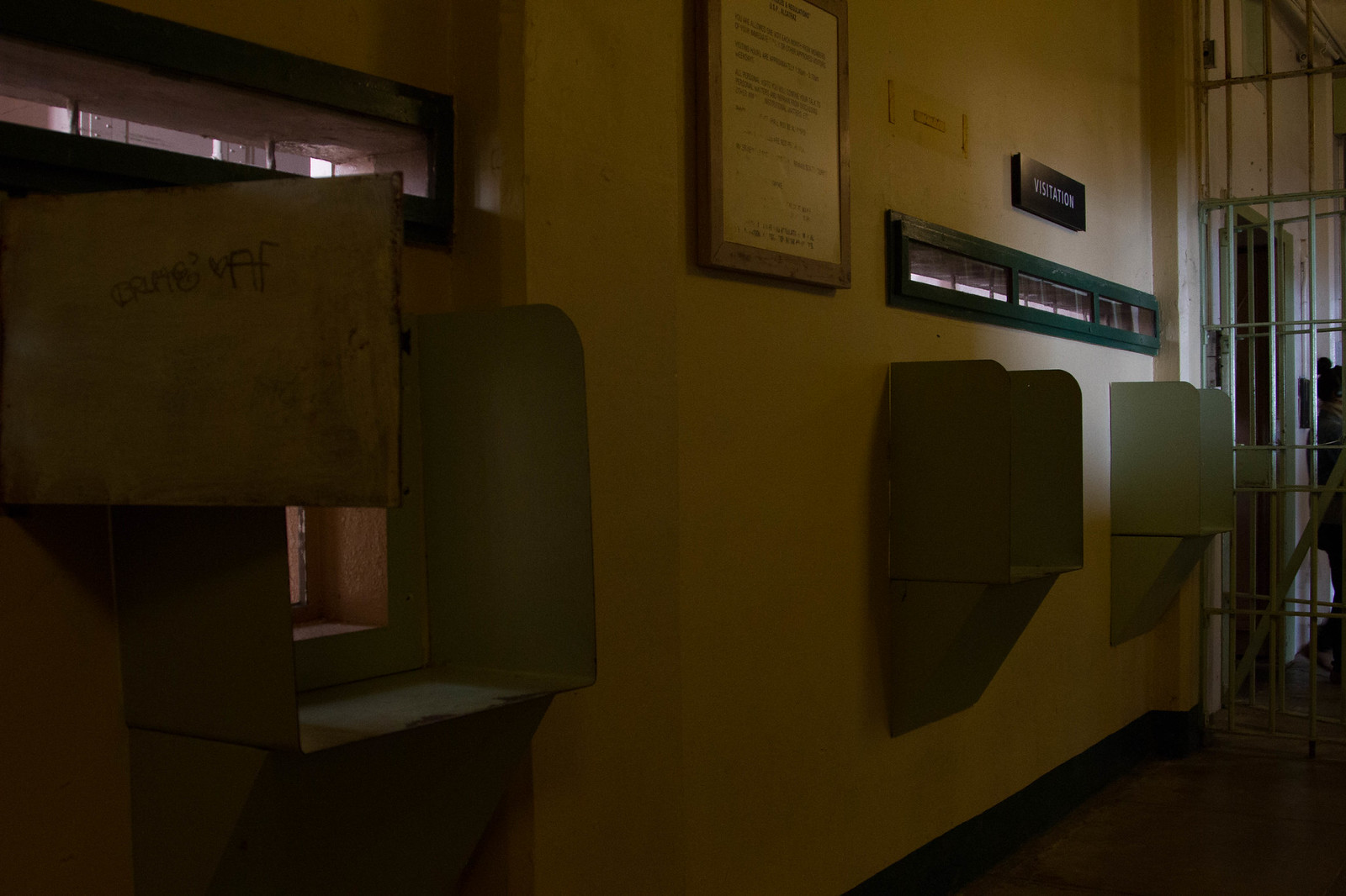 Row of dim visitor booths along a yellow prison wall beneath a "VISITATION" sign at Alcatraz.