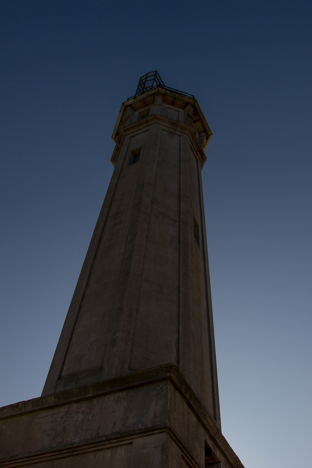 The octagonal Alcatraz lighthouse tower viewed from below against a deep blue dusk sky.
