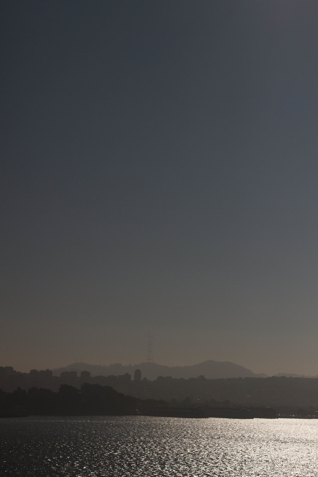 Hazy San Francisco skyline silhouette with Sutro Tower, seen across shimmering bay water at dusk.