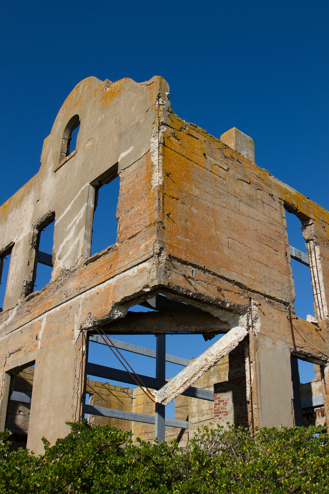 Roofless, lichen-stained shell of the Warden's House on Alcatraz, its empty windows framed against a deep blue sky.