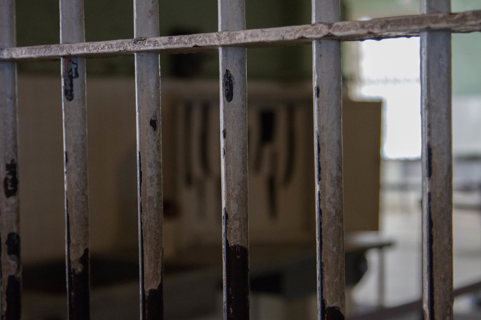 Kitchen knives silhouetted against a shadow board, seen through the worn bars of the Alcatraz prison kitchen.