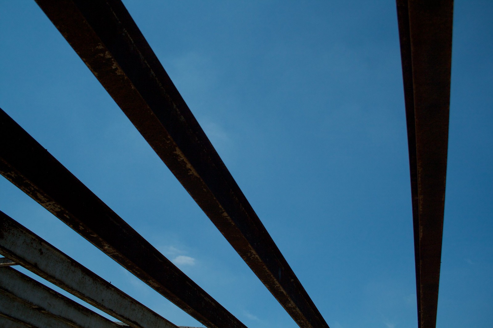 Rusted metal beams silhouetted against a clear blue sky, radiating outward like fingers.