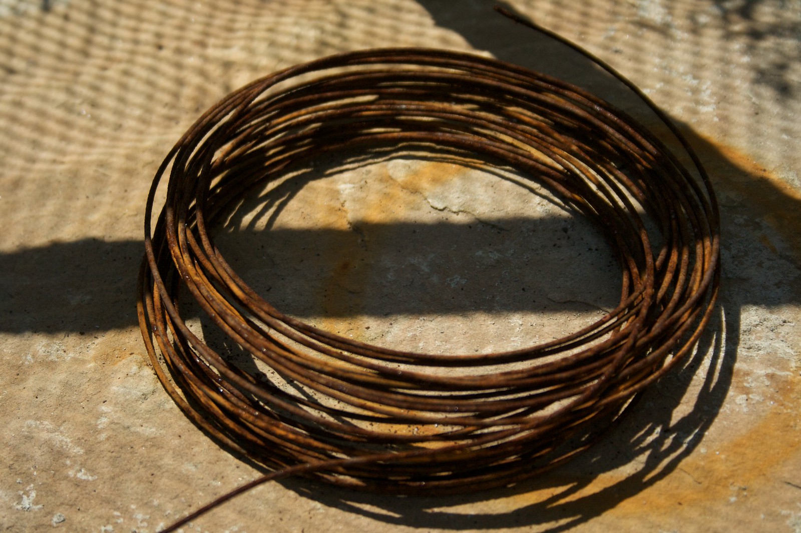Rusty coil of copper wire resting on a sunlit stone surface, casting long shadows