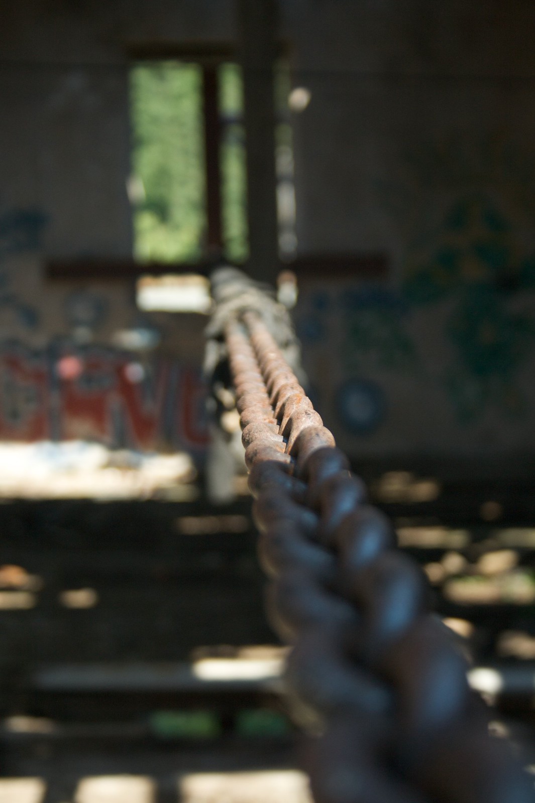 A rusted twisted metal cable stretches toward a bright window in a graffiti-covered abandoned building.