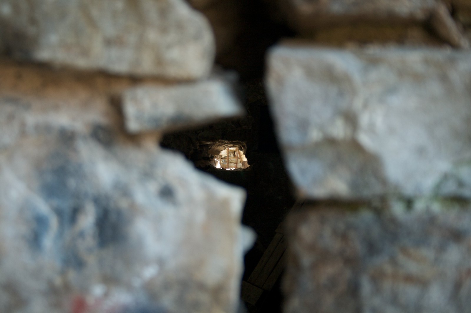 Daylight glimpsed through a small hole in a rough, weathered stone wall, blurred boulders framing the gap.