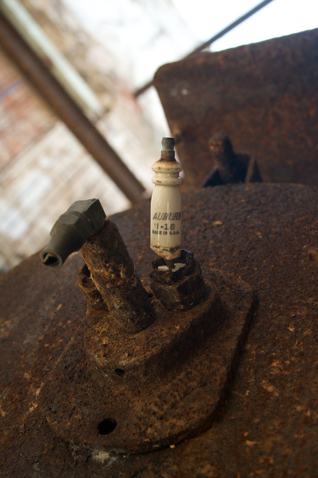 Cream ceramic "Auburn 1-18" spark plug on a heavily rusted engine block in an abandoned building.