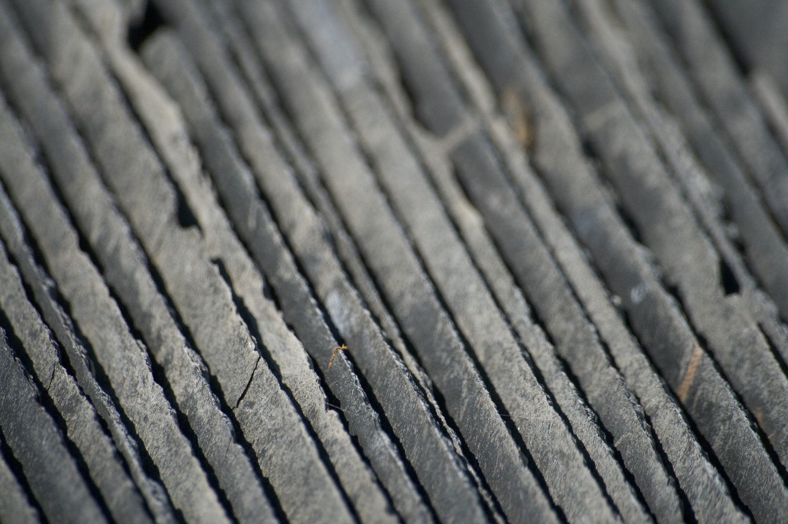 Close-up of layered gray slate rock with diagonal ridges and thin cracks catching the light.