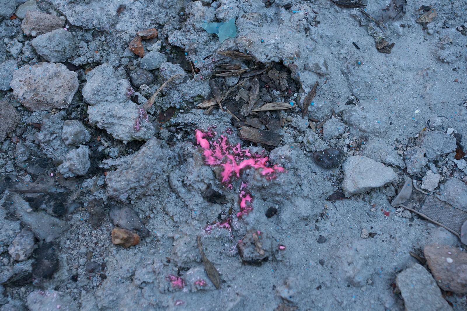 A splash of bright pink spray paint splattered across gray gravel, dirt, and wood chips.
