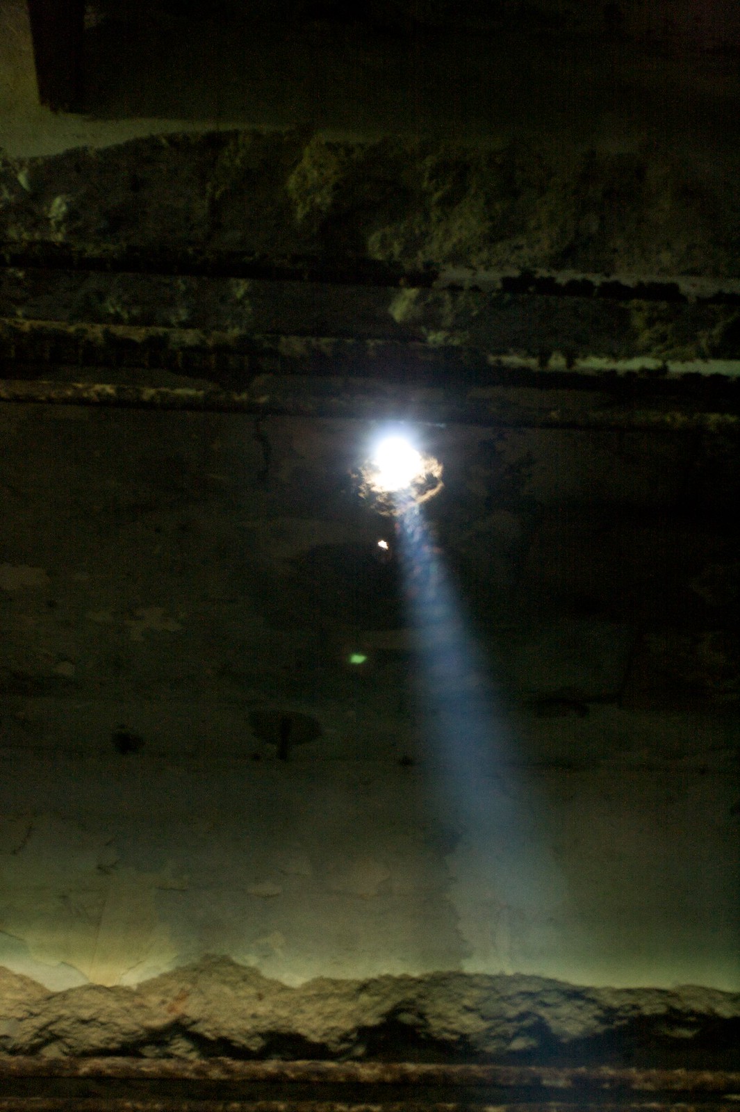 A shaft of light streams through a hole in the crumbling, weathered wall of a dark abandoned building.