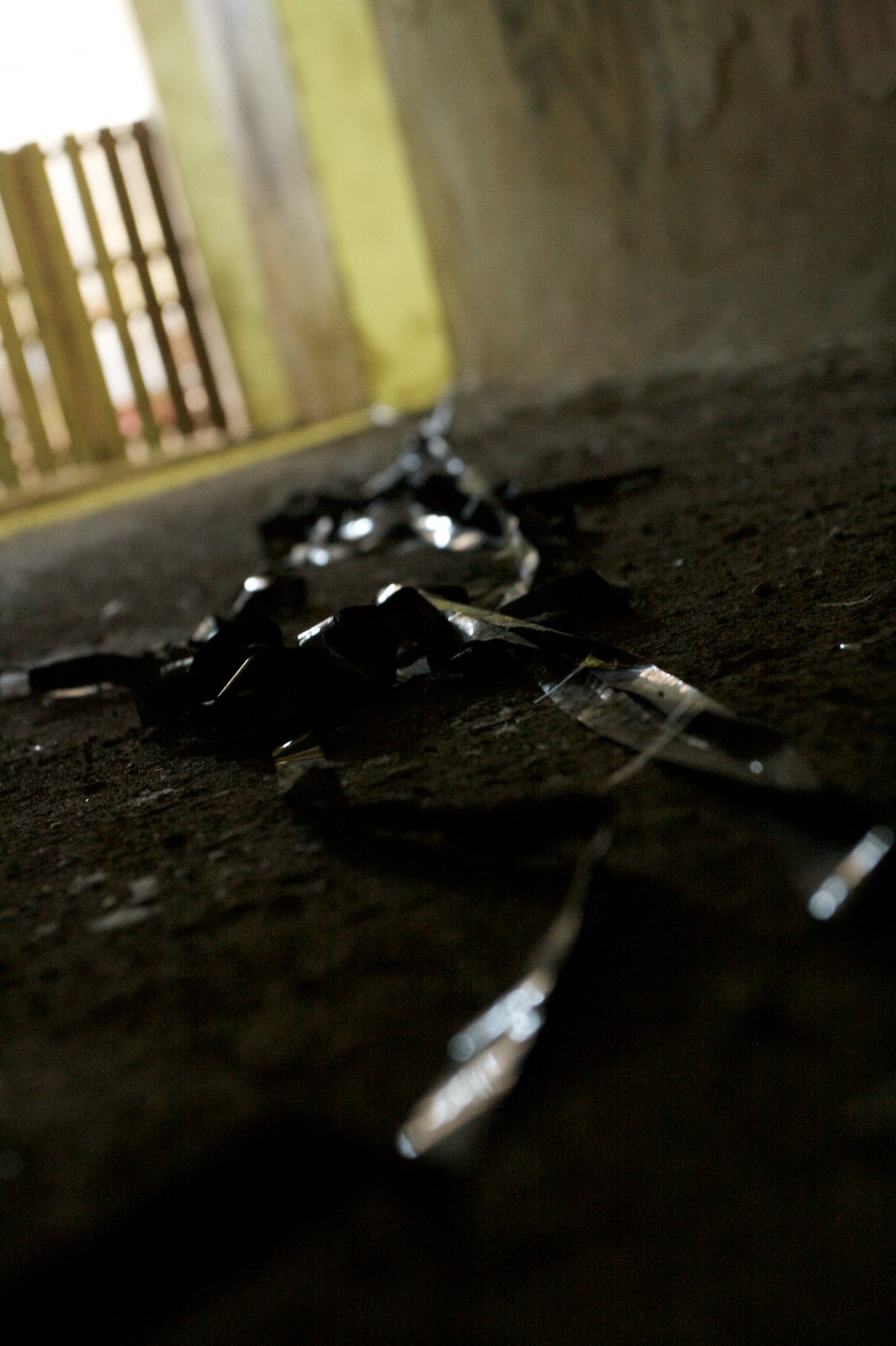 Curled strips of exposed black film tape scattered on a dusty concrete floor beside a sunlit barred window.