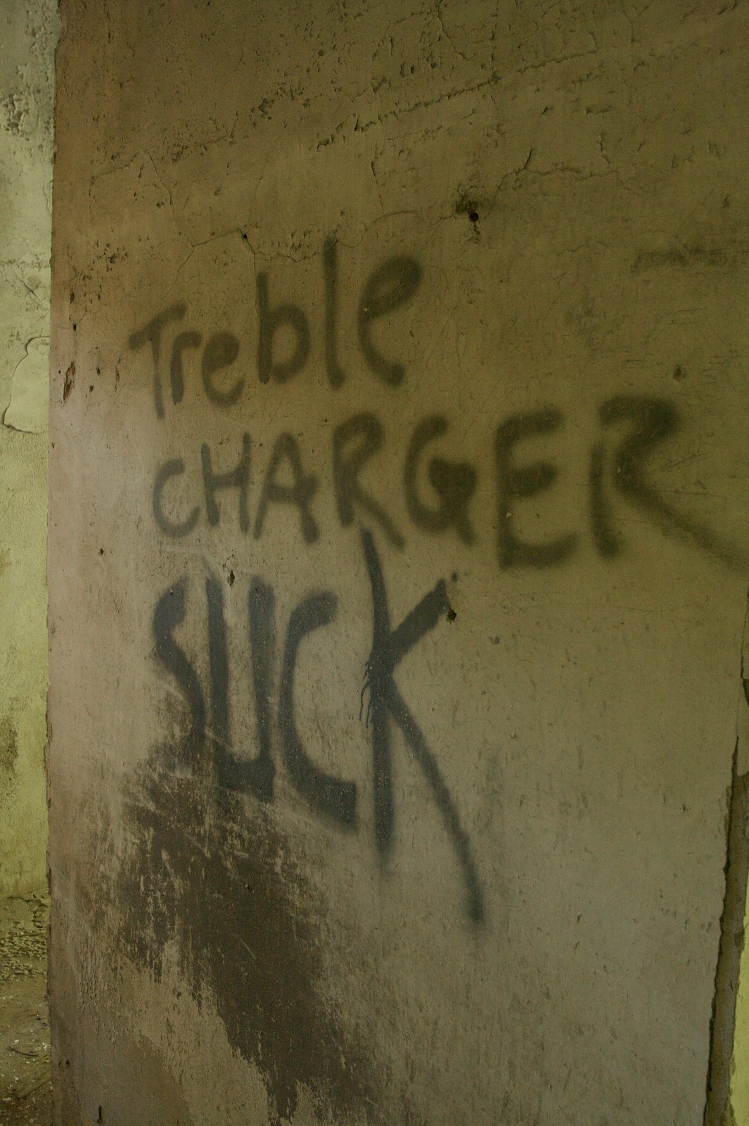 Graffiti reading "Treble Charger Suck" spray-painted in black on a cracked, weathered concrete wall.