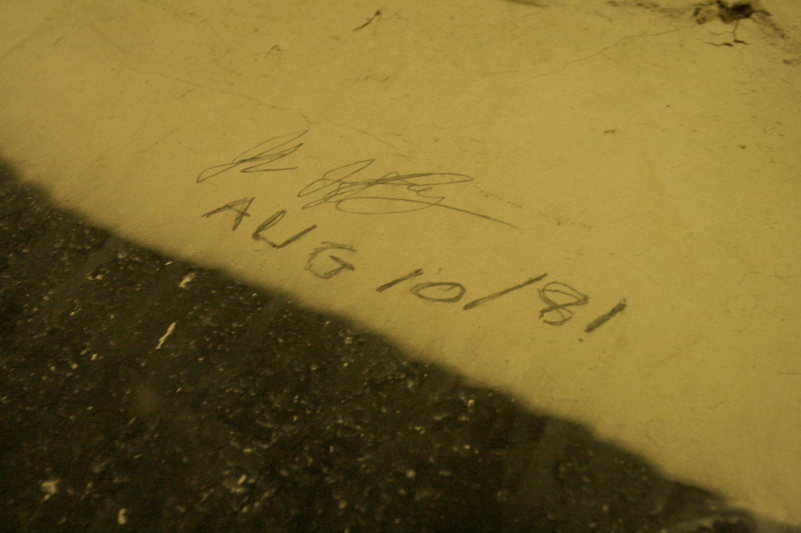 A pencil signature and the handwritten date "AUG 10/81" scrawled on a weathered plaster wall.