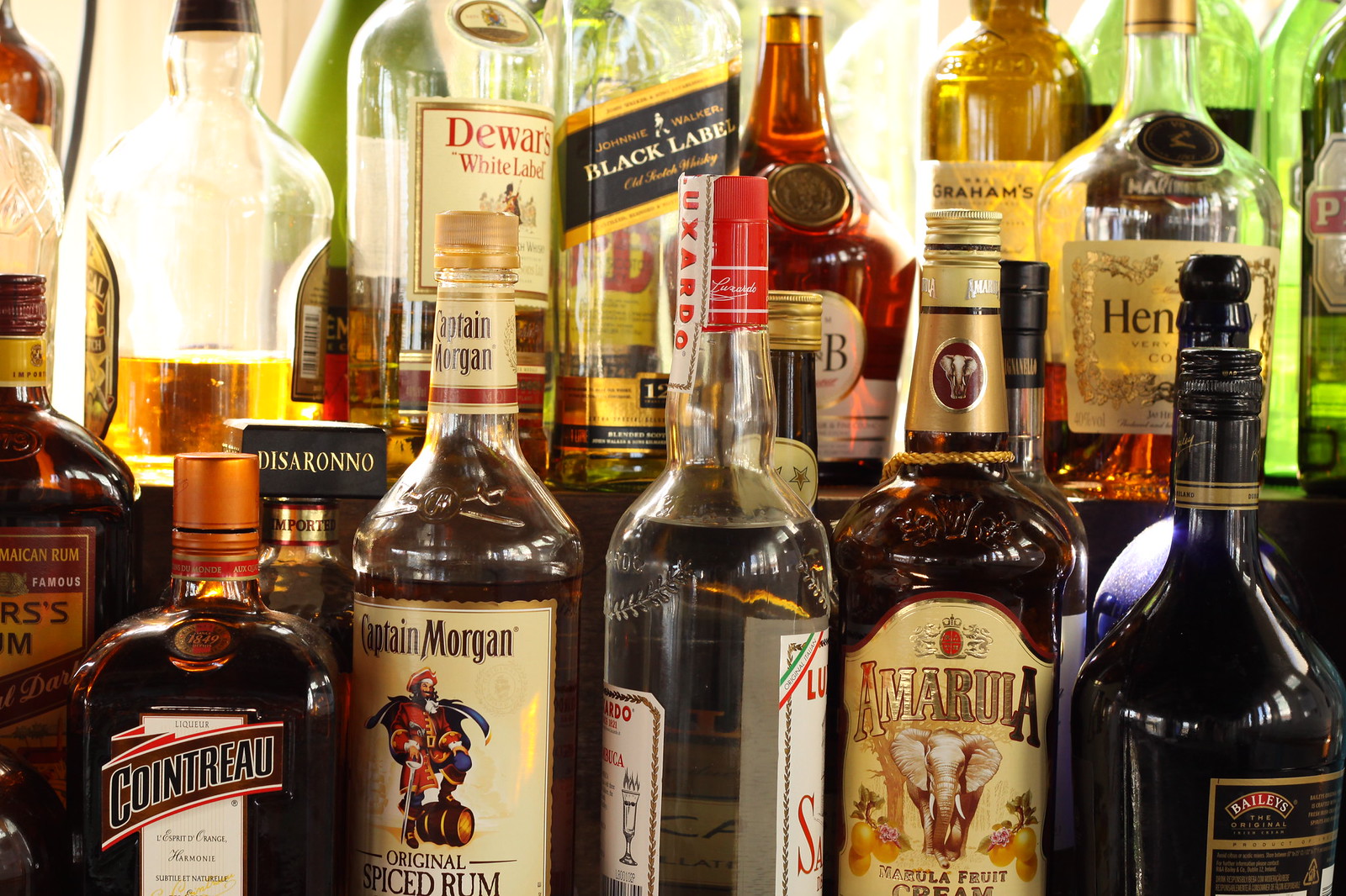 Backlit bar shelf crowded with liquor bottles including Captain Morgan, Cointreau, Amarula, Dewar's and Johnnie Walker Black Label.