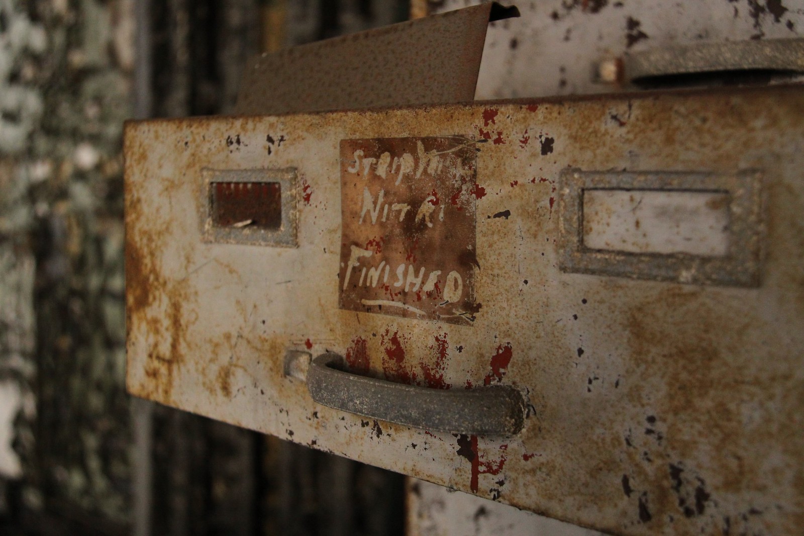 Rusted metal filing cabinet drawer in an abandoned office, its handwritten label reading "FINISHED.