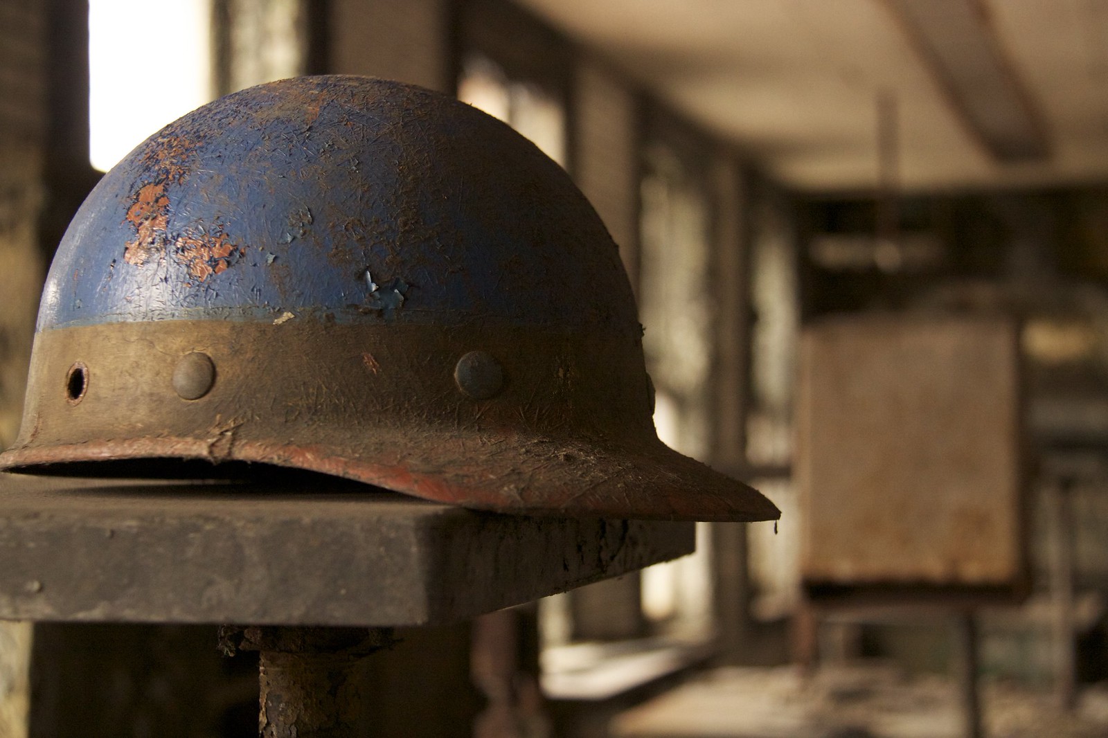 A weathered blue hard hat coated in dust rests on a dusty ledge in an abandoned industrial office.
