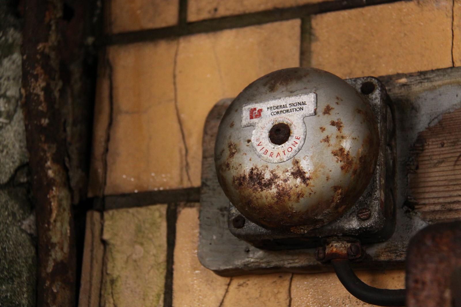 Rusted Federal Signal Corporation "Vibratone" alarm bell mounted on a cracked, tiled wall.