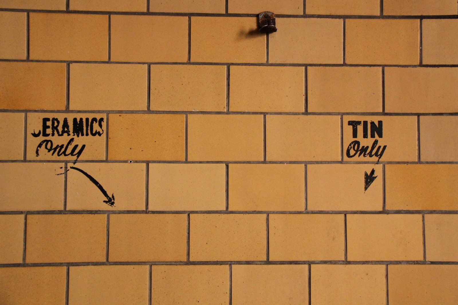 Yellow tiled wall stenciled with "Ceramics Only" and "Tin Only," each with a black arrow pointing down.