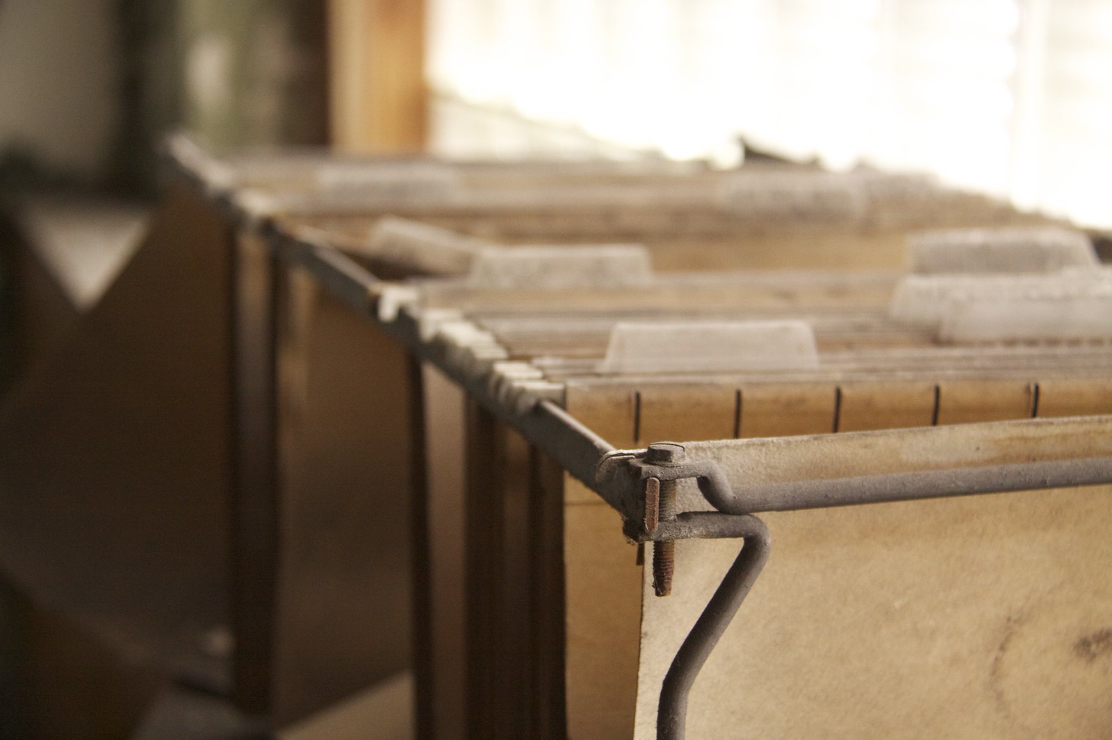Dusty file folders with worn tab dividers in an open drawer, backlit by a bright window.