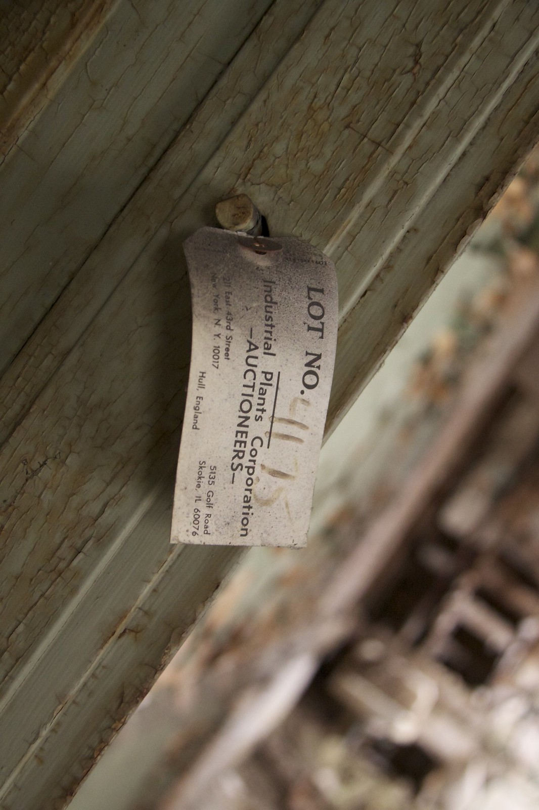 Auction tag reading "LOT NO." from Industrial Plants Corporation Auctioneers, nailed to peeling paint on abandoned equipment.
