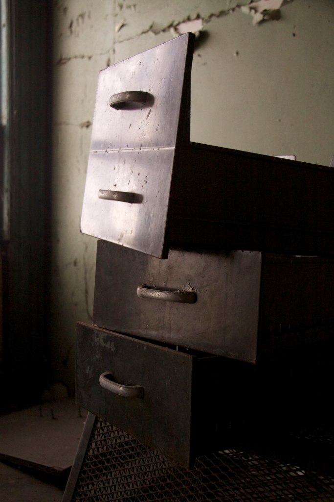 Rusted metal filing cabinet drawers hang open at odd angles in an abandoned, decaying office