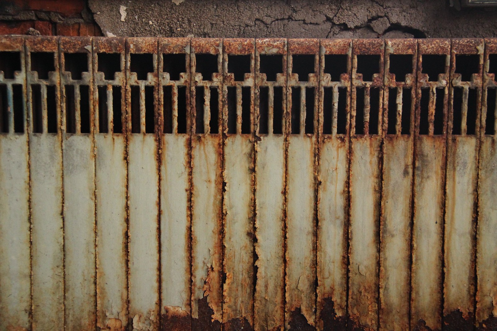 Rusted cast-iron radiator with peeling paint against a cracked concrete wall.