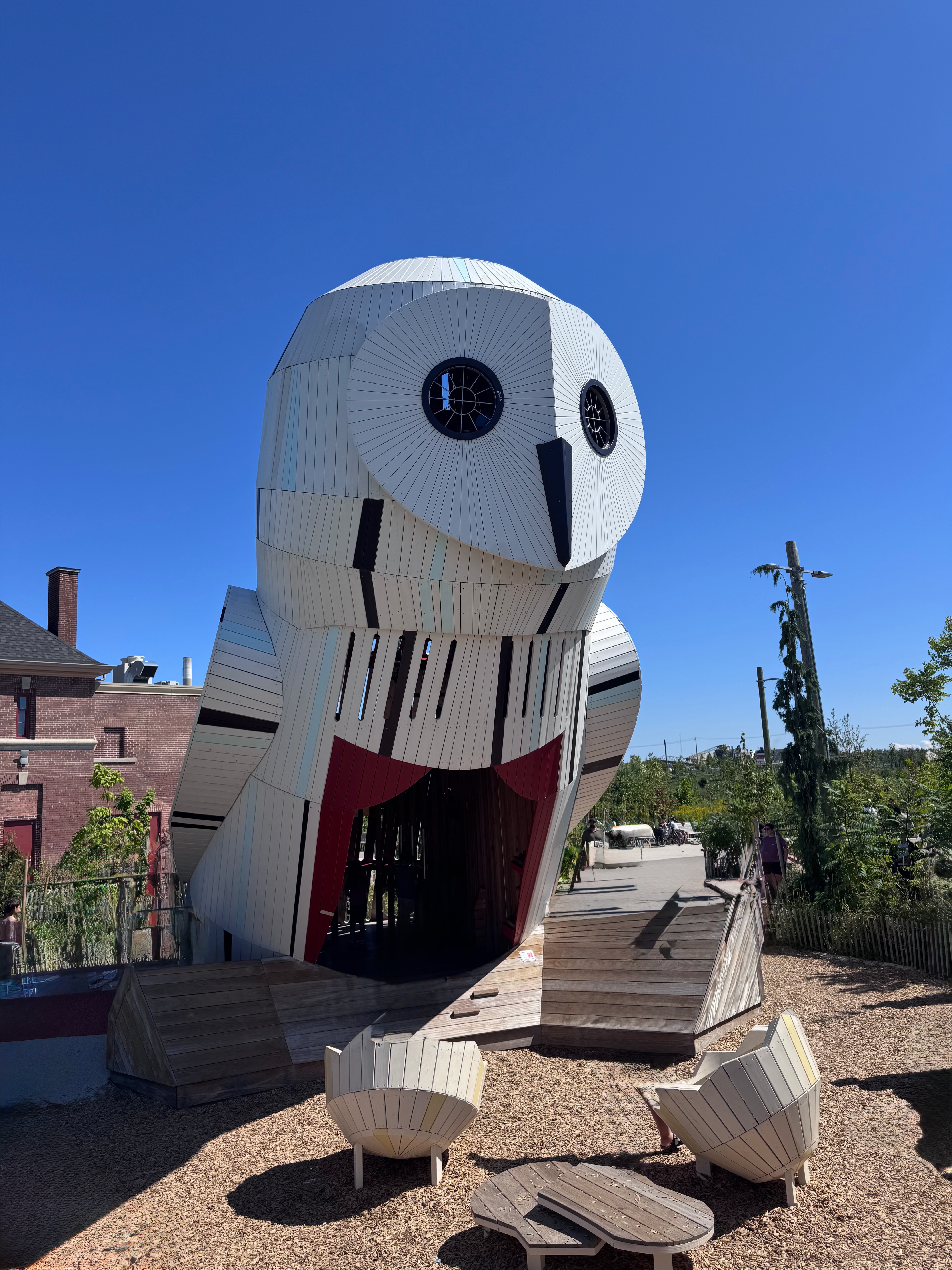 A giant wooden owl-shaped playground structure with round eyes stands under a clear blue sky.
