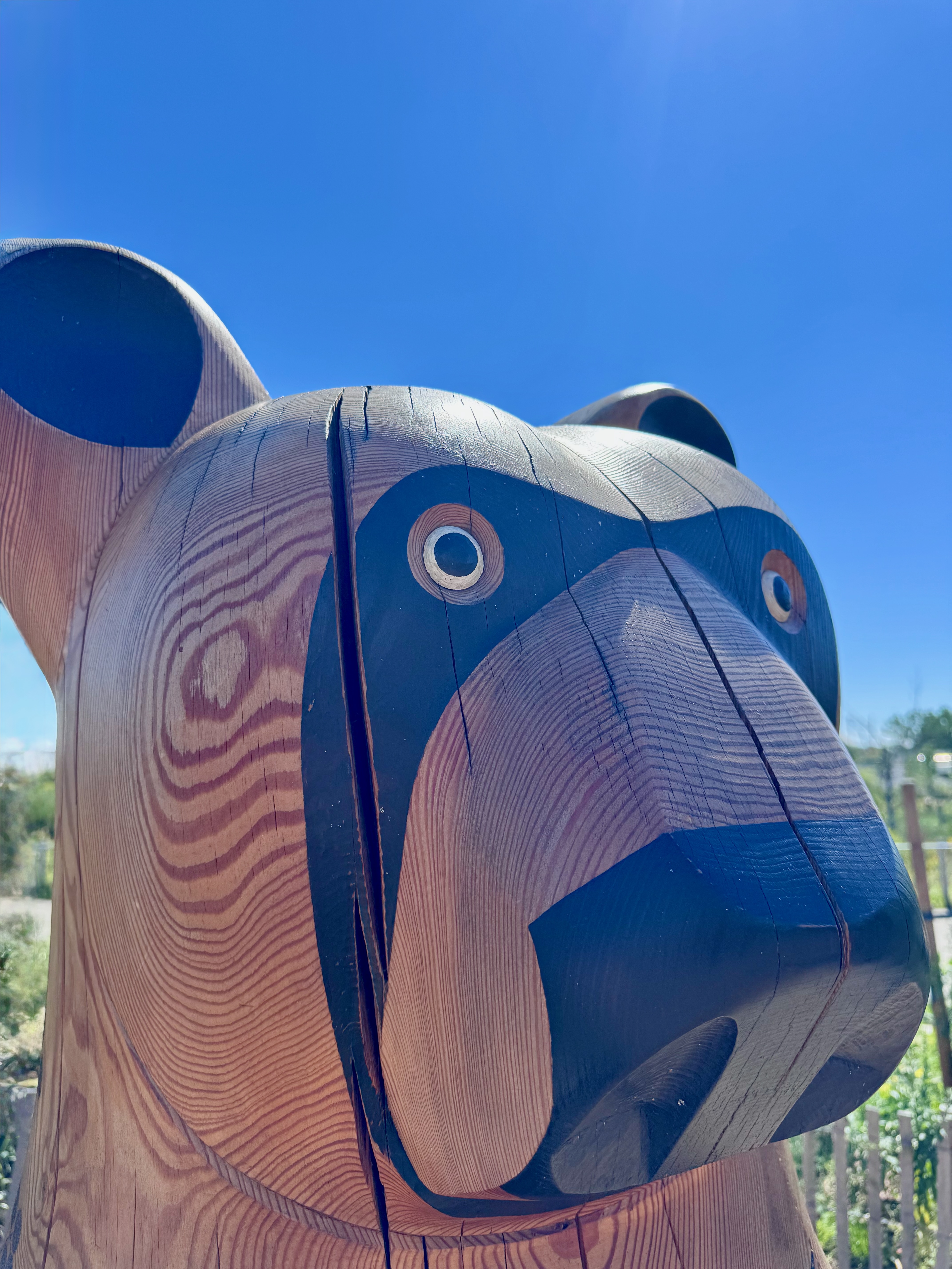 Carved wooden bear sculpture with painted black face and eyes against a bright blue sky.