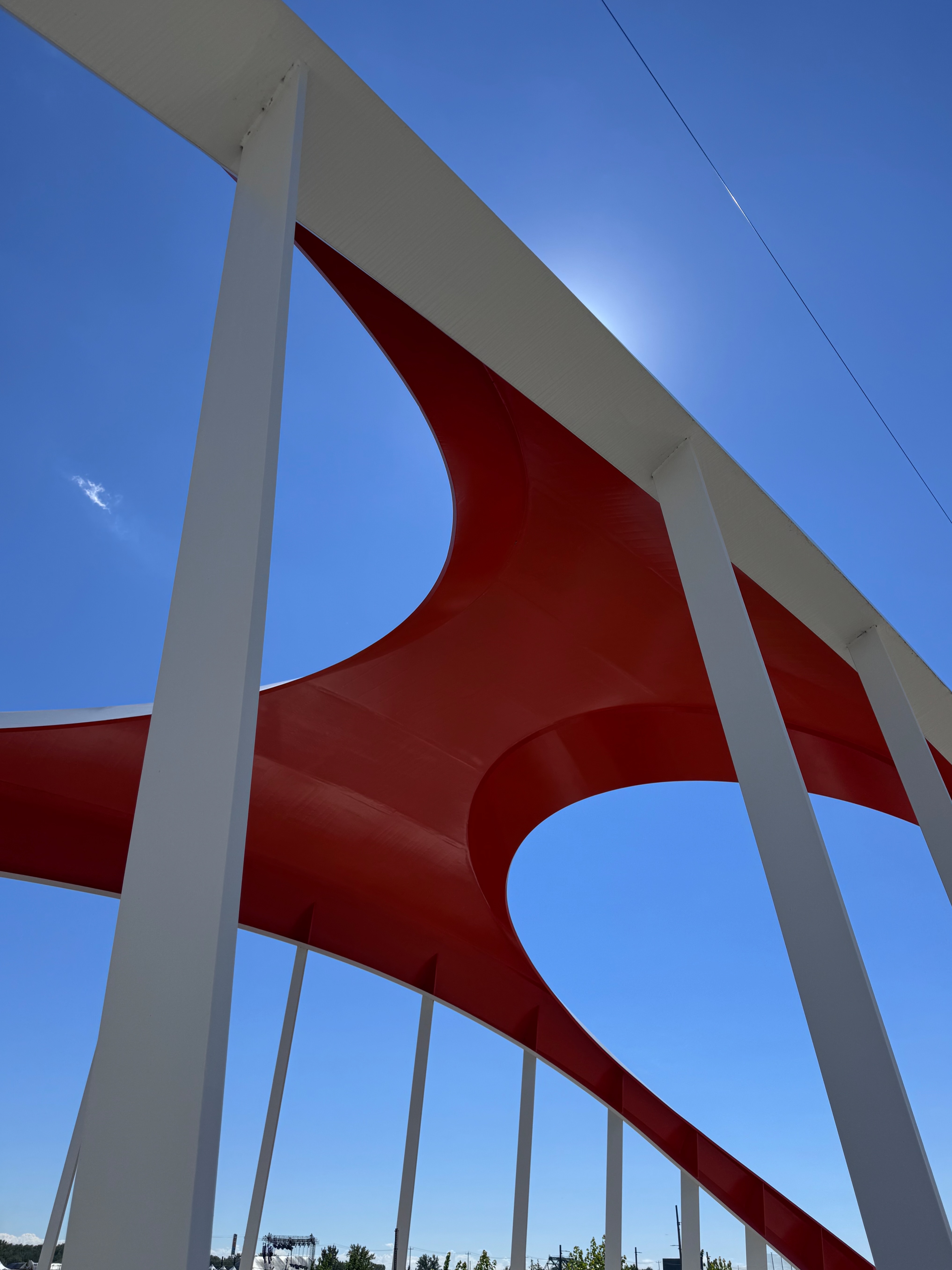 Curving red-and-white sculptural bridge structure against a bright blue sky.