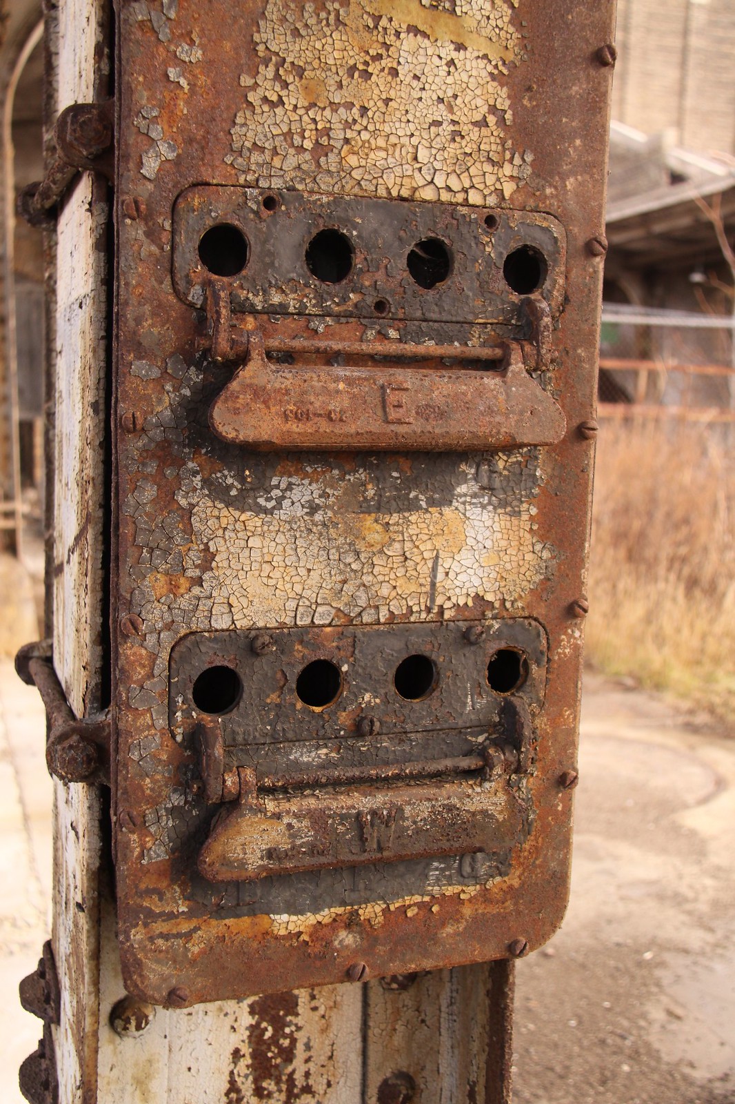 Rusted railway signal control panel with peeling paint and levers labeled "E" and "W" at an abandoned terminal.