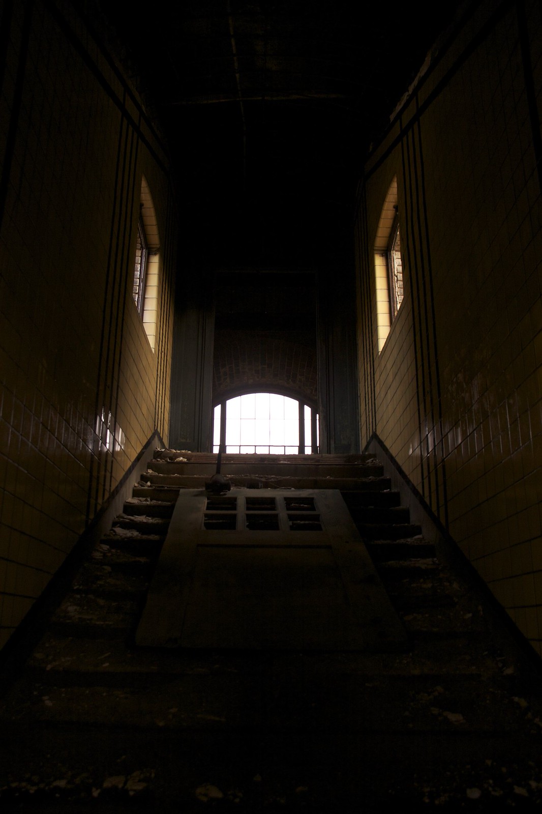 Sunlight glows through an arched window at the top of a dark, tiled stairwell in the abandoned Buffalo Central Terminal.