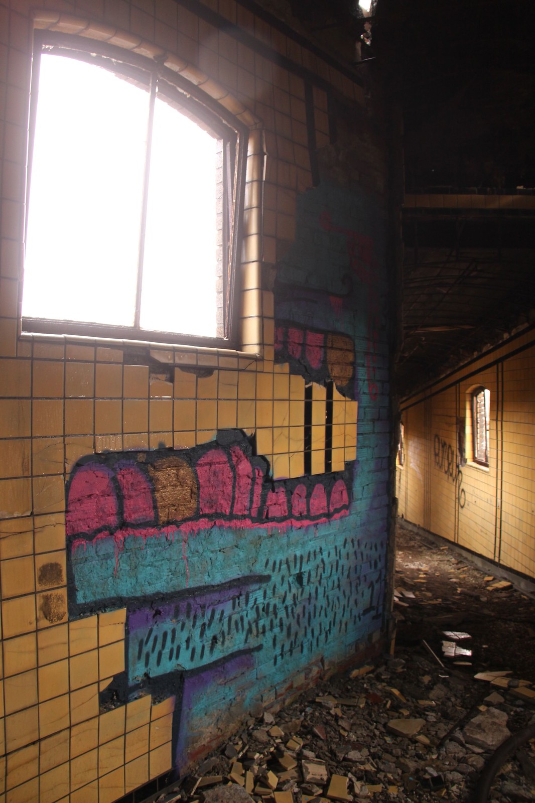 Colorful graffiti mural on the tiled walls of a fire-damaged, abandoned room with rubble covering the floor.