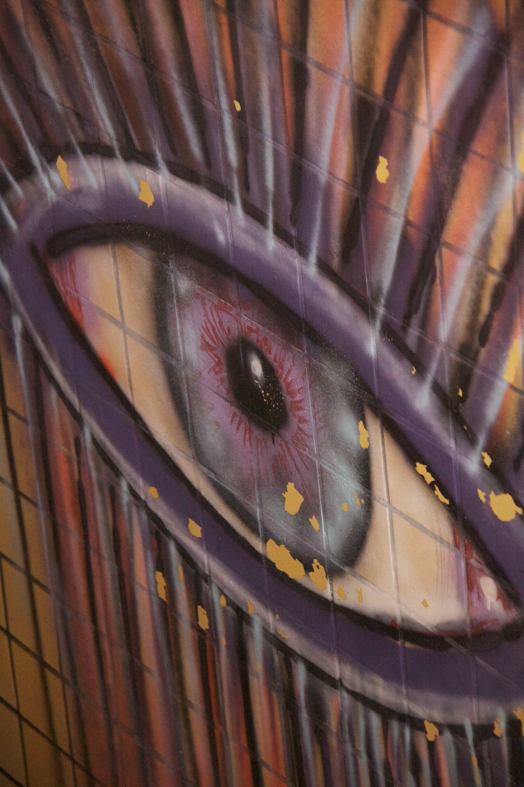 Close-up of a spray-painted mural of a human eye on cracked tiled wall, with dripping paint and gold flecks.