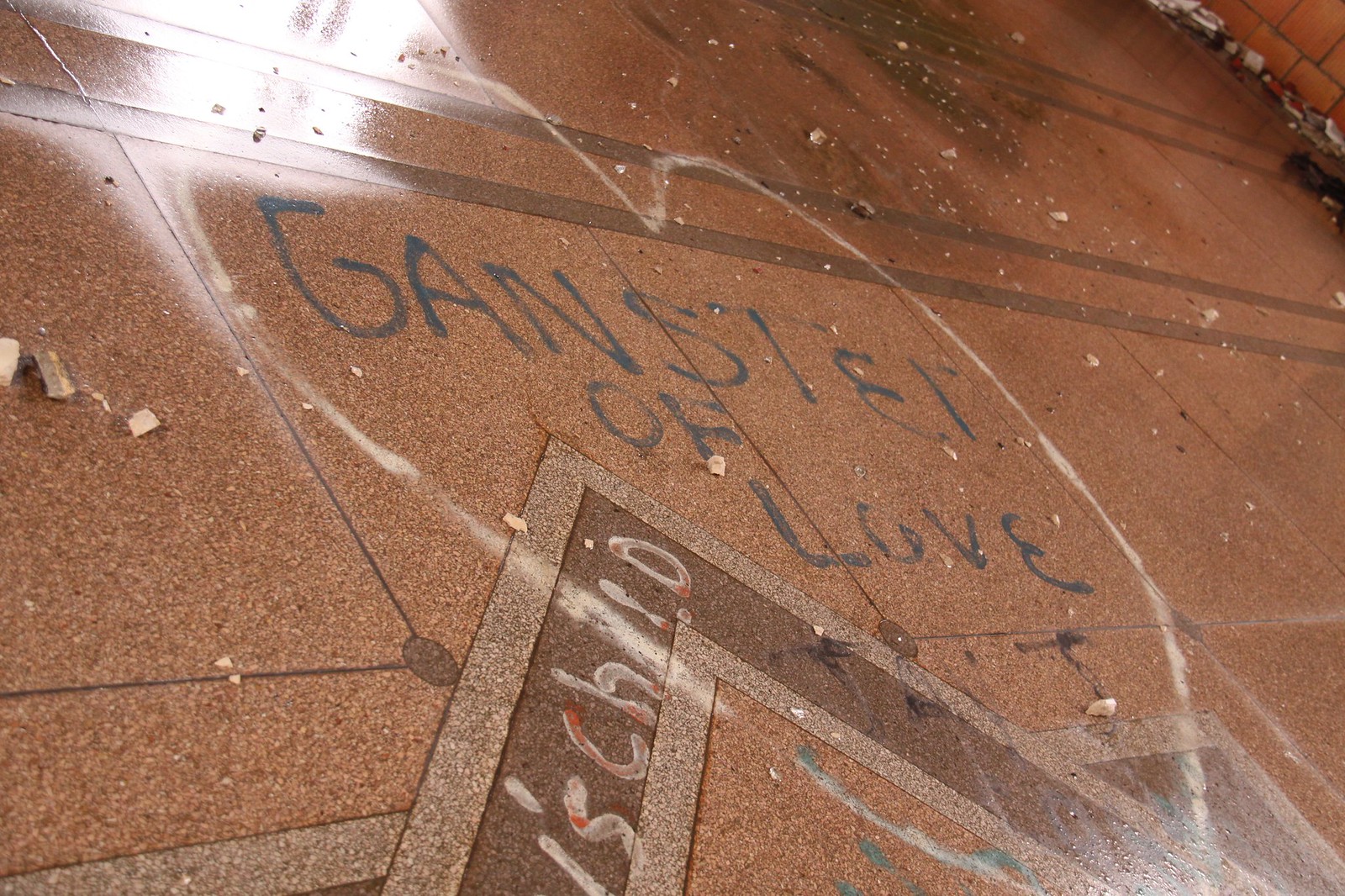 Ganster of Love" graffiti scrawled on a weathered terrazzo floor scattered with plaster debris.
