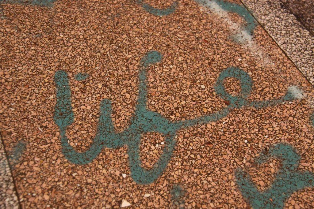 life" spray-painted in teal cursive across a weathered terrazzo floor