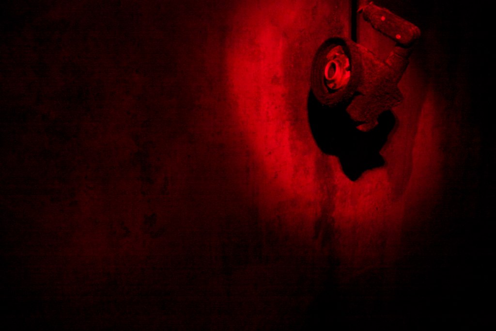 A camping headlamp glowing bright red against a dark concrete wall in near-total darkness.