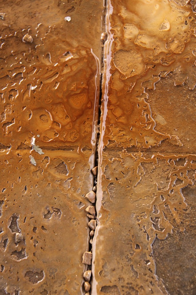 Rust-colored water pooling and staining a weathered stone floor along a pebble-filled seam.