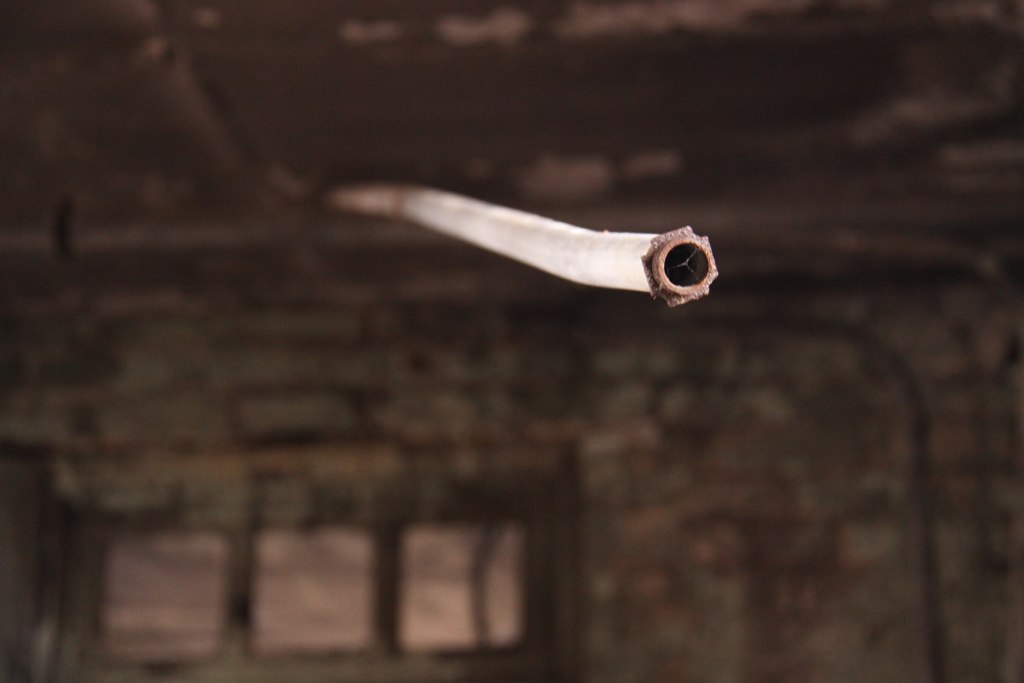 A rusted, broken conduit pipe juts out against the decaying interior of an abandoned building.
