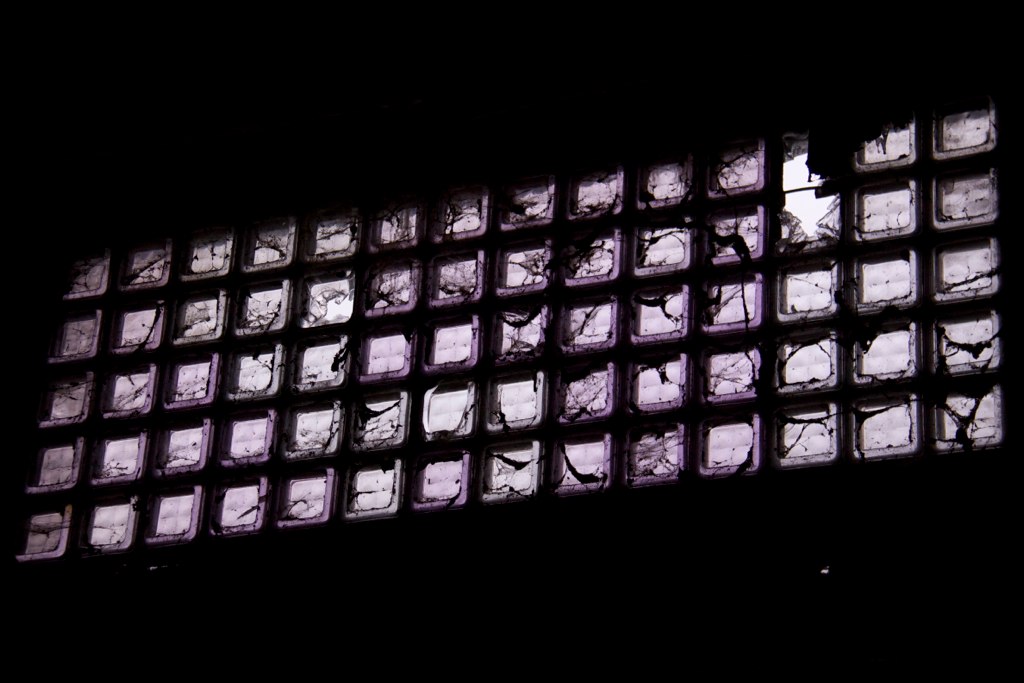 A grid of cracked, purple-tinted glass block windows glowing against a dark wall.