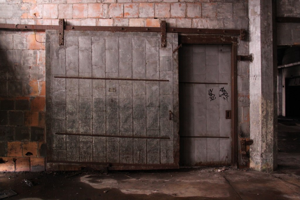 A large metal sliding fire door numbered 45 in a derelict brick industrial hall, graffiti tags nearby.