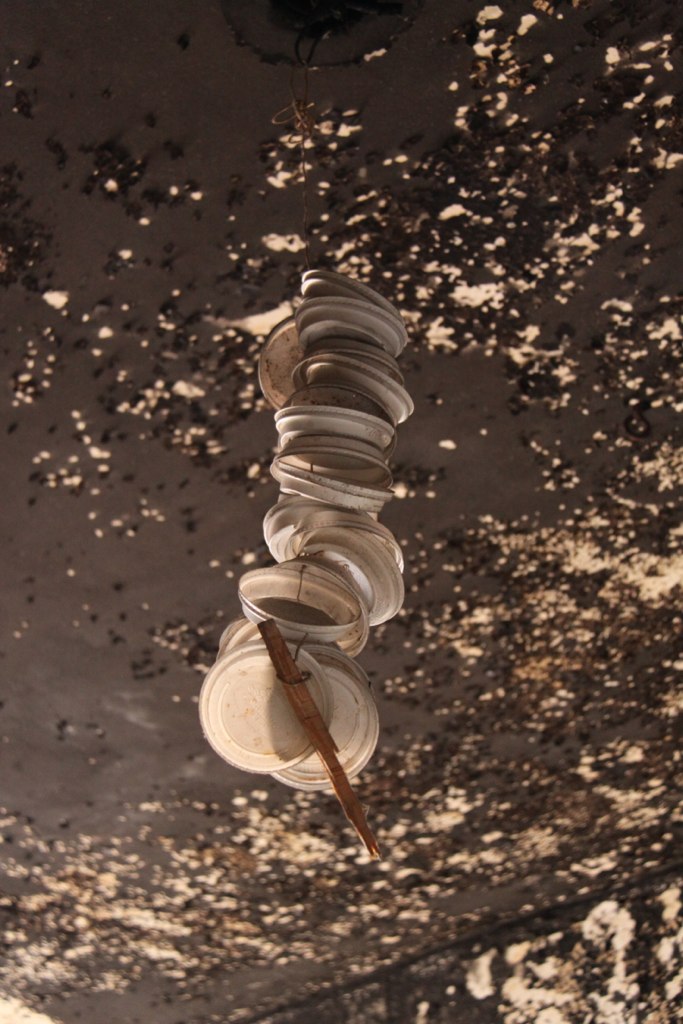 Coffee-cup lids threaded on a wire dangle from a peeling, water-stained ceiling in an abandoned building.