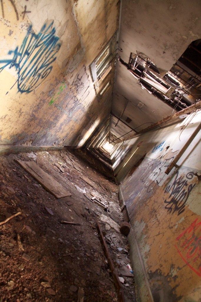 Graffiti-covered elevator shaft in a derelict building, plunging past debris-strewn floors below.