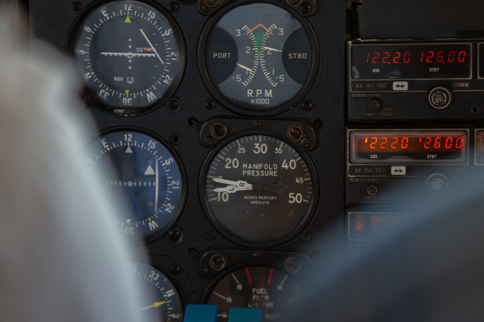 Vintage aircraft cockpit instrument panel showing RPM, manifold pressure gauges and radios tuned to 122.20 and 126.00.