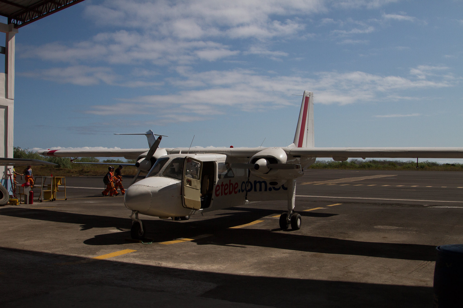 Small white Emetebe twin-propeller plane parked on a Galápagos airstrip under a blue sky.